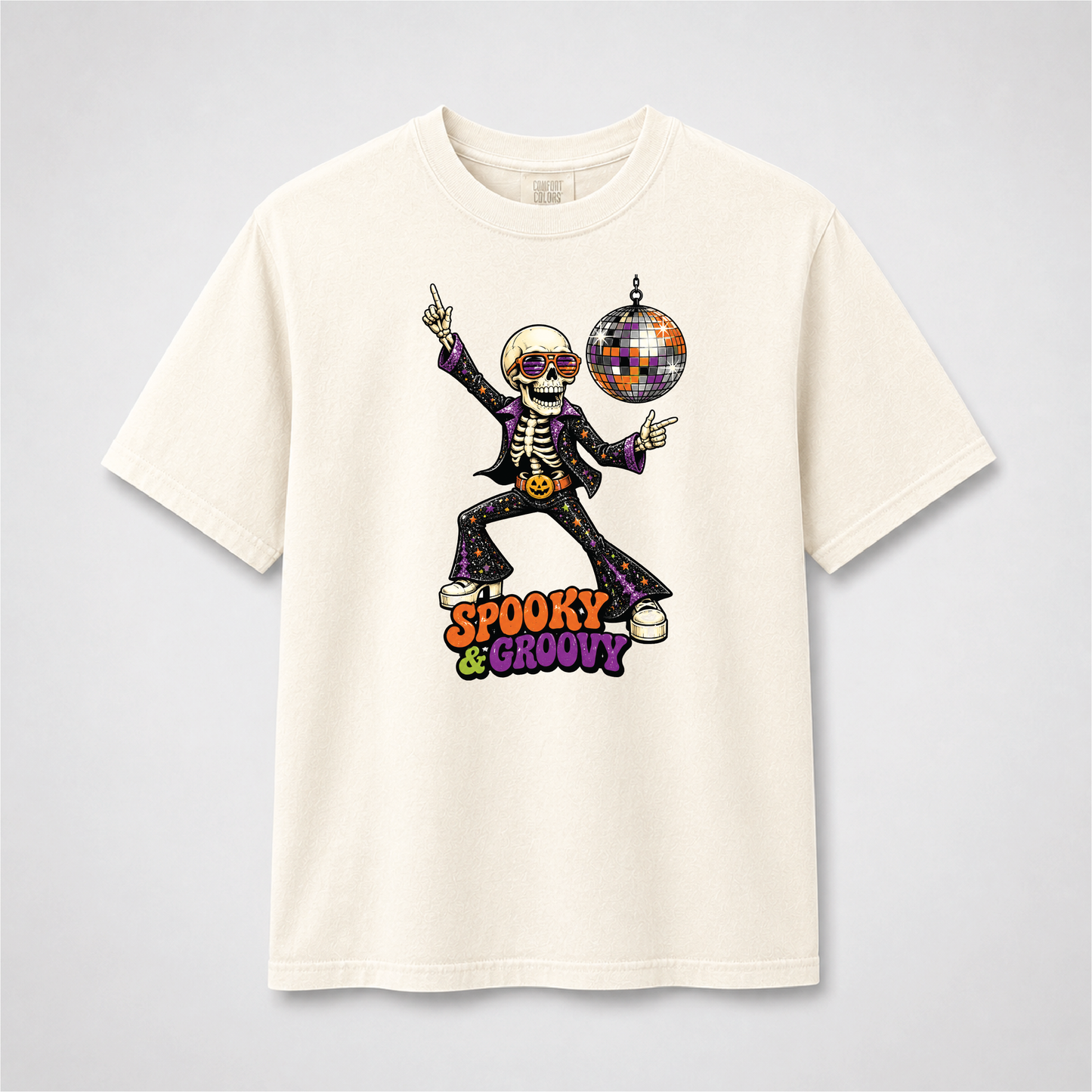 Ivory Comfort Colors T-shirt featuring a dancing disco skeleton in retro sunglasses beside a colorful disco ball with Spooky & Groovy lettering.